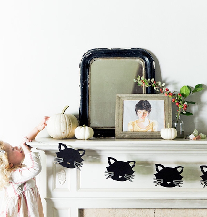 activité halloween maternelle, une cheminée blanche avec guirlande en papier de silhouettes têtes de chats noires, miroir et cadre dessins fille, citrouilles decoratives