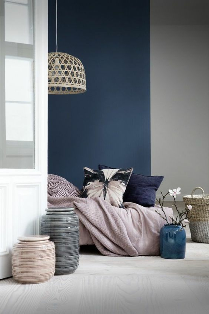 chambre adulte bleu avec un mur entier en bleu gris et des murs en blanc et gris clair avec des coussins sur le lit en bleu et violet