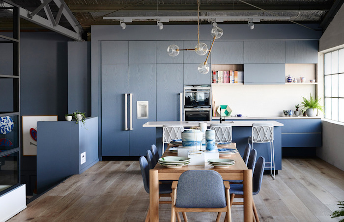aménager une petite cuisine avec façade couleur bleue et crédence blanche, ilot central bleu, salle à manger avec table en bois massif et chaises en bois avec assise vioeltte
