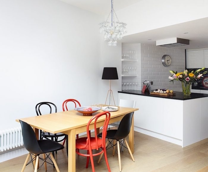 aménager une petite cuisine blanche, mur en briques blanchis, ilot avec plan de travail noir, chaises noires et rouges en bois et table en bois, parquet clair