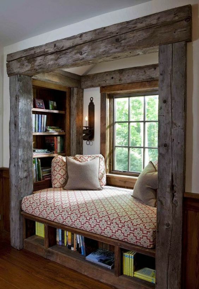 chambre de 9m2 dans une niche en bois gris clair rude avec lit au matelas en rouge et blanc, des étagères avec des livres, et bougeoir mural en fer forgé