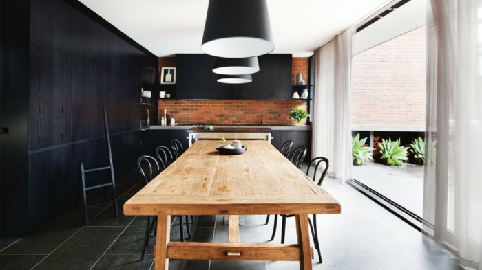 aménager une petite cuisine, facade meuble cuisine noire, suspensions noires au dessus d une table en bois, entourée de chaises metalliques, sol carrelage gris et credence cuisine en briques