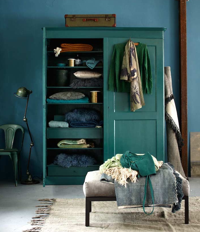 armoire bleu petrole peinture, adossé à un mur bleu foncé avec des accents déco vert emeraude, chaise et lampe verte, malle vintage