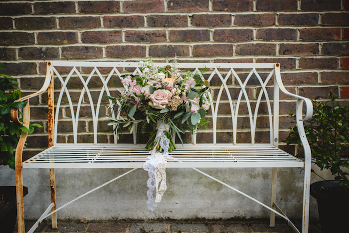bouquet champetre de mariée, décorée de dentelle blanche sur un banc metallique rouillé, mur de fond en briques