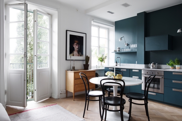 deco nordique, cuisine avec meubles en bleu foncé et étagères murales, table à manger blanche avec chaises noires
