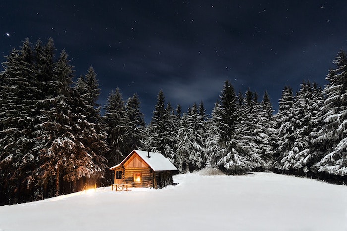 paysage hiver fond ecran, montagne enneigée, petite cabane avec lumière à l intérieur, arbres, sapins couverts de neige