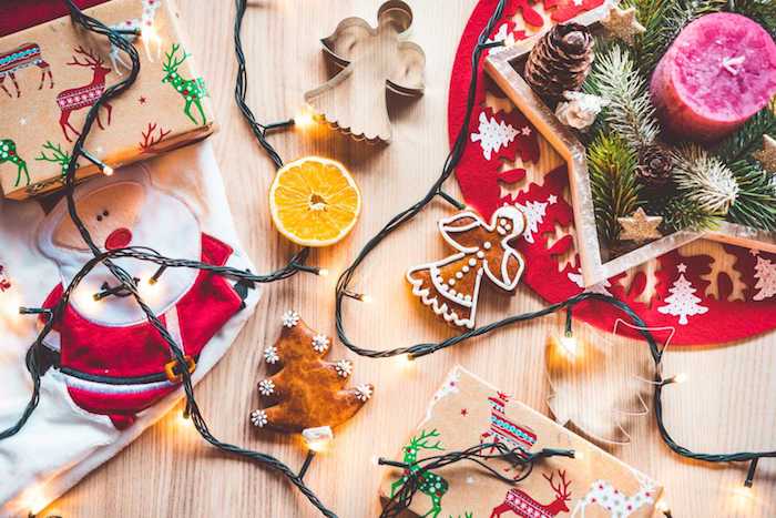 fond d écran de noel, centre de table noel en etoile bois avec branches et pommes de pin et bougie rose à l interieur, guirlande lumineuse, biscuits et cadeaux emballage en papier craft à motifs festifs