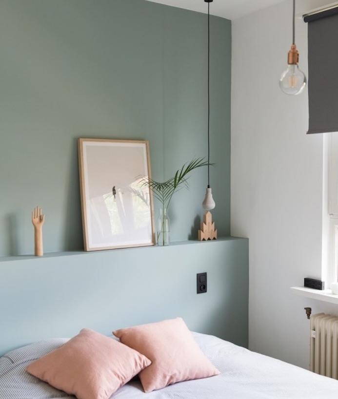 chambre scandinave avec des murs repeints en couleur vert de gris de teinte celadon, linge de lit blanc à petites rayures noires, coussins rose, suspensions originales