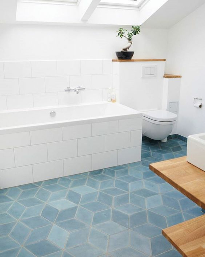 nuance de bleu gris sur le carrelage d'une salle de bains sous pente aux meubles blancs avec baignoire revêtue en carrelage blanc
