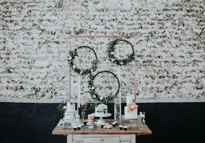 couronnes avec fleurs blanches et feuillages sur une table vintage en bois brut, gâteau fleuri, mur en pierre sur le fond