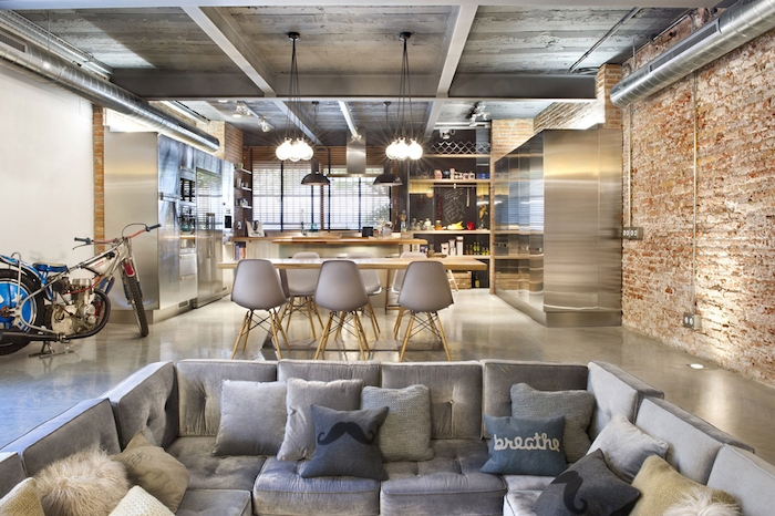 cuisine americaine style industriel, cuisine gris et bois ouverte sur salle à manger chaises scandinaves et table en bois, canapé d angle gris, mur en briques