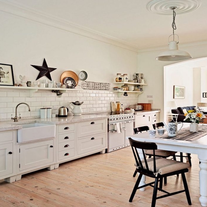 cuisine rénovée avec meuble cuisine et carrelage blanc, parquet en bois clair, etageres ouvertes avec vaisselle blanche, table blanche entourée de chaises marron