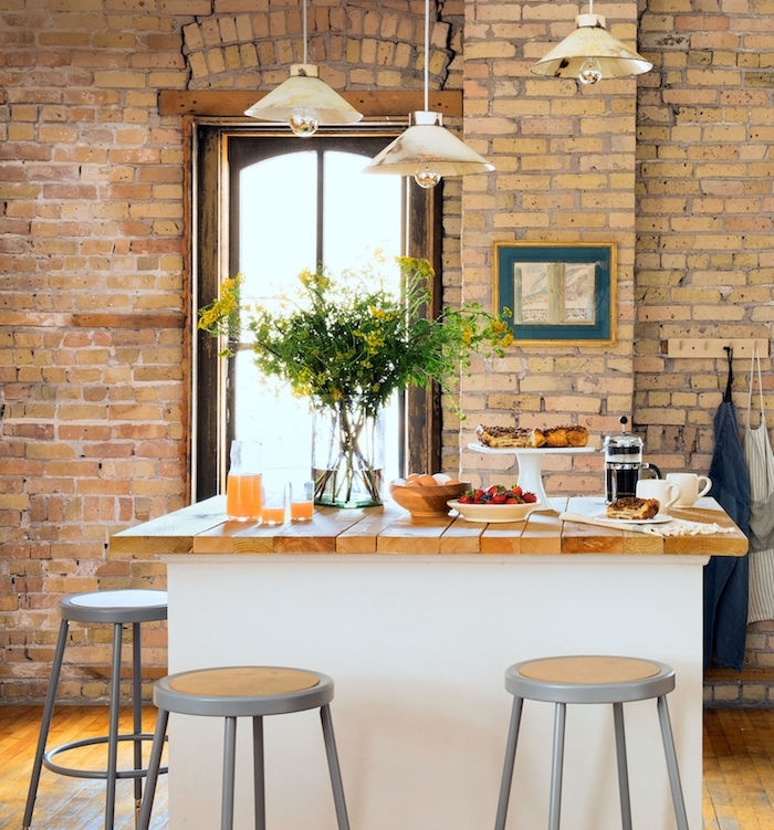 modele de cuisine campagne rustique avec mur en briques, suspensions vintage elegantes, ilot central blanc avec plan de travail bois, petit déjeuner campagnard