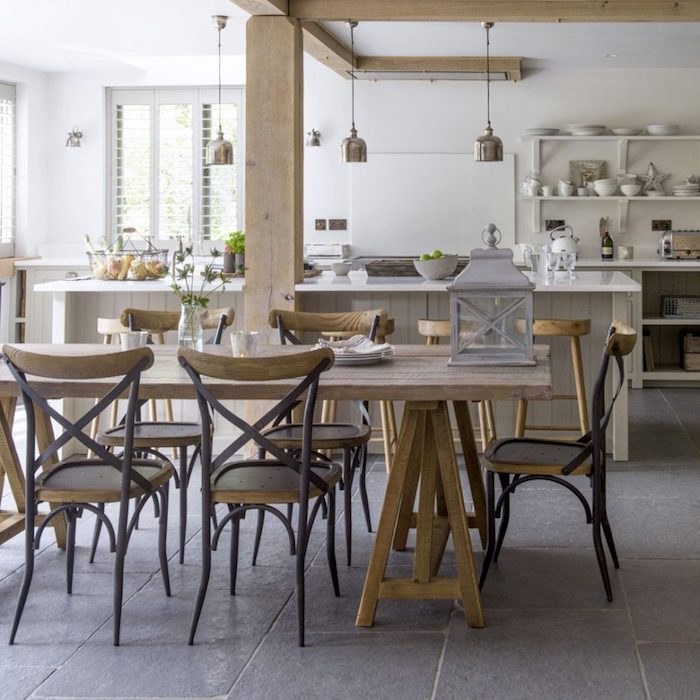 modele de deco cuisine rustique avec poutres apparentes, chaises et table en bois brut, sol dallage effet beton, ilot central gris clair et etageres blanches