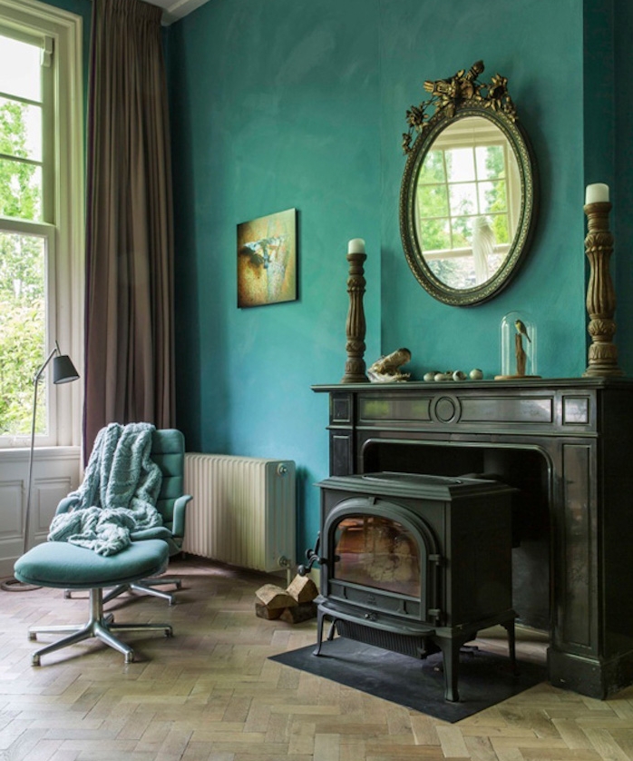 modele de deco salon bleu canard, mur couleur pétrole, cheminée noire rétro, parquet clair, chaise pivotant bleu ciel, rideau marron, miroir baroque