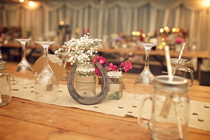 deco table mariage rustique champetre, chemin de table en jute, centre de table en fer à cheval, pots en verre décorés de dentelle et jute avec des fleurs de champs