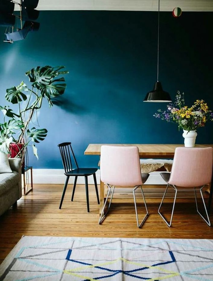 deco salle a manger bleu petrole, table en bois, chaises rose et noir, parquet bois, tapis gris à motifs geometriques, plante verte