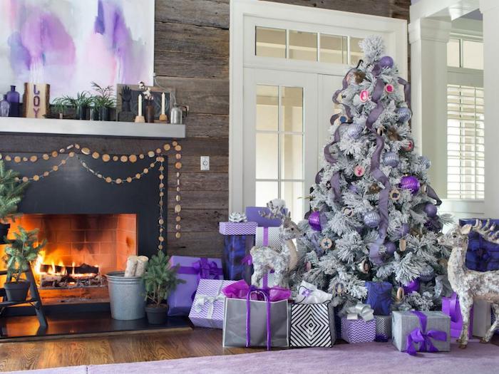 modele de sapin de noel blanc avec decoration de boules de noel et guirlandes mauve, gris et violet, paquets cadeaux gris, cheminée moderne en bois