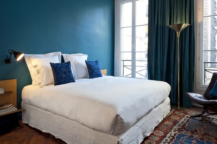 idée déco chambre adulte, mur d accent bleu foncé, rideau bleu paon, linge de lit blanc avec des coussins decoratifs bleus, tapis oriental, parquet marron