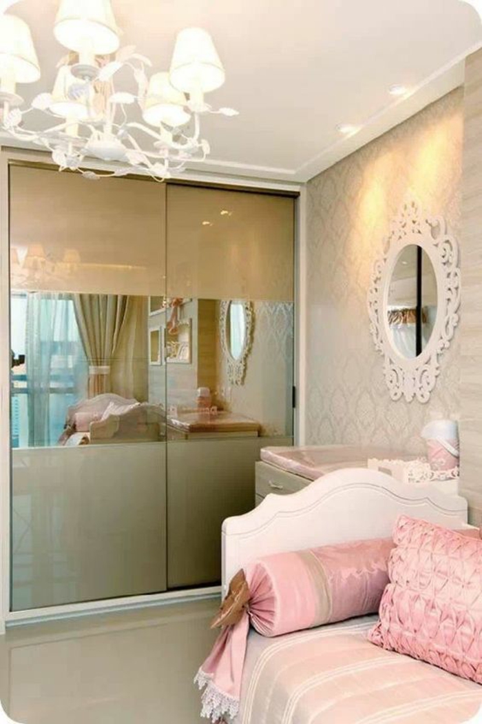 deco petite chambre adulte en style romantique, avec grand lustre, miroir blanc en style baroque, armoire aux portes coulissantes en couleur or, lit blanc avec des coussins roses en forme carrée et en forme de bonbon 