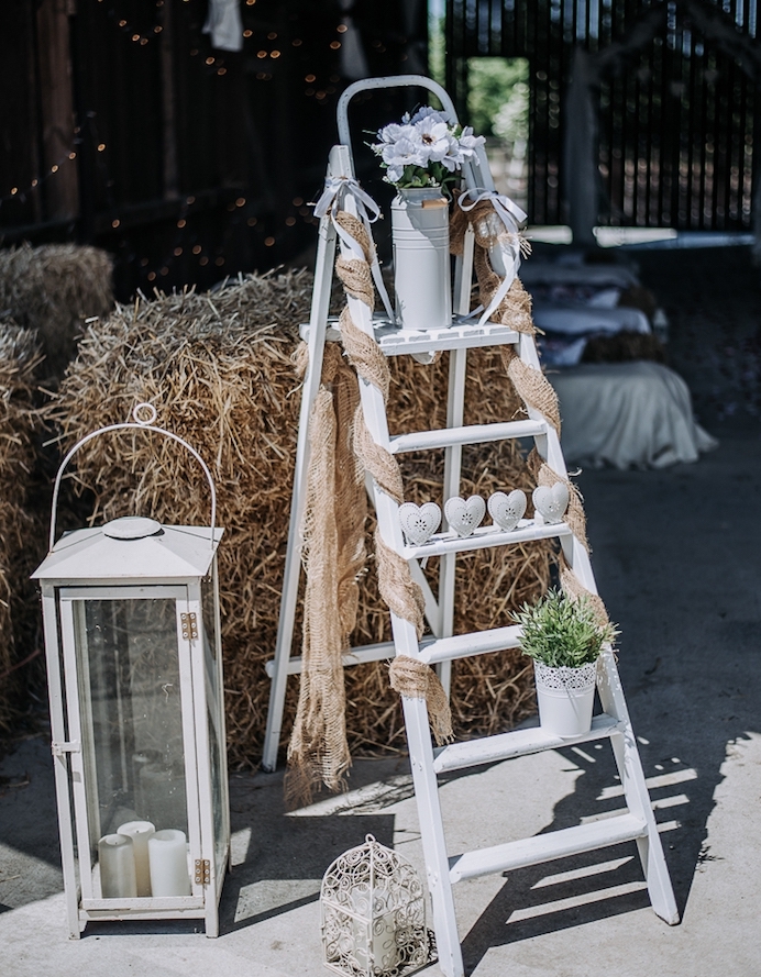 decoration mariage champetre, echelle decorative blanche, coeurs blancs, pot à lait fleuri et grande lanterne avec des bougies à l intérieur, meules de foin
