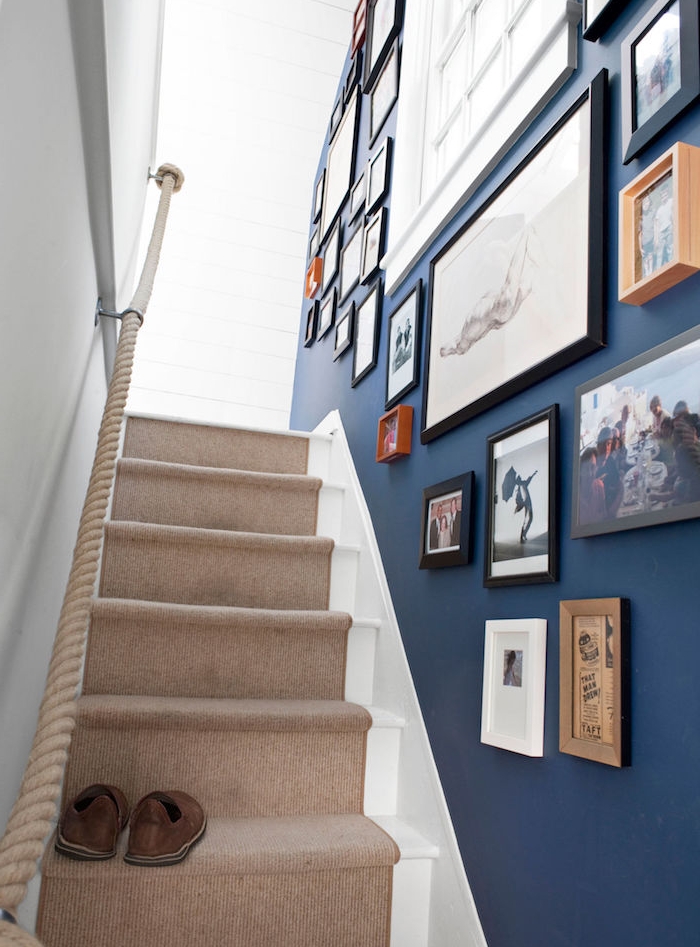 déco montée d escalier, mur repeint en bleu marine avec deco de cades dessins, peintures, photos, tapis beige et main courante en corde, style bord de mer 