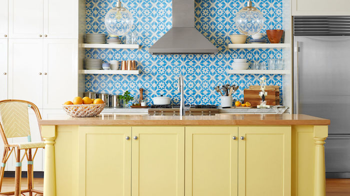 cuisine rénovée avec ilot central jaune et plateau en bois, etageres ouvertes blanches sur un fond carrelage mosaique bleu et blanc
