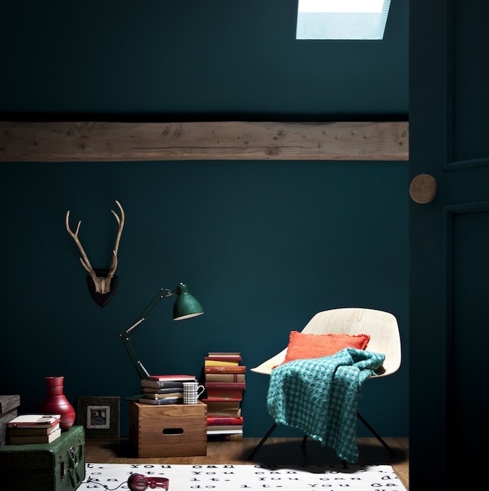 modele d intérieur couleur bleu pétrole, chaise scandinave, pile de livres, coffret vert émeraude, tapis blanc à lettres noires, poutre apparente, deco de bois de cerf