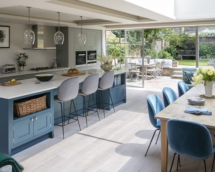 modele de cuisine avec bar couleur bleue, facade meuble cuisine grise, aspirateur en inox, parquet gris, table basse en bois et chaises bleues