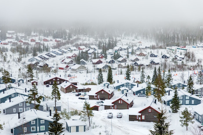 fond d écran hiver, village enneigé au peid d une montagne en suede, maisons cabanes bleues, marrons et rouges
