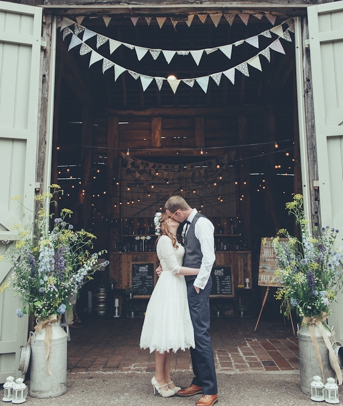 mariage champetre dans une grange, guirlande fanions, couple mariés, lanternes blanches et pots à lait fleuris, guirlande lumineuse