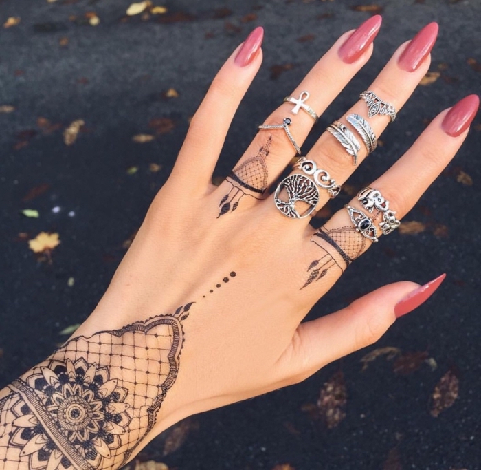 dessin henné, manucure aux ongles longs et vernis rouge, henné noir à design dentelle et bracelet sur la main féminine
