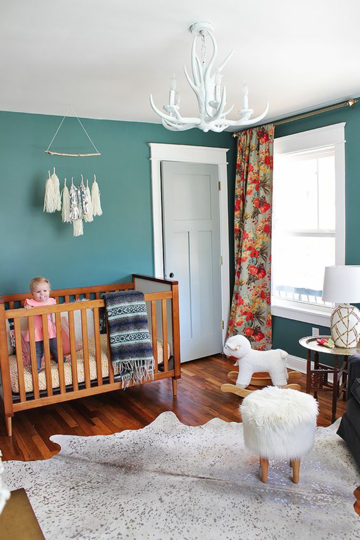 chambre bébé en bleu canard avec plafond en blanc et un tapis imitation peau d'animal en blanc luminaire en style baroque avec des cornes
