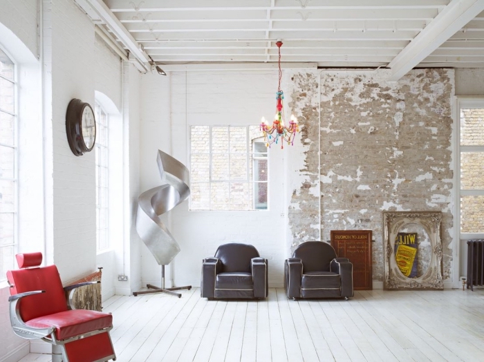 salon en style loft industriel aux murs blancs et plancher en bois peint blanc, fauteuils en cuir marron et rouge