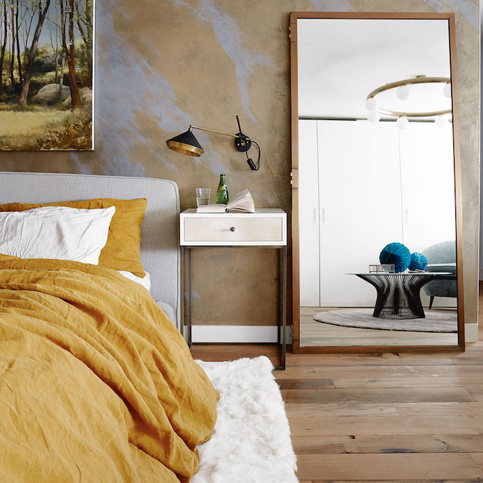 idée pour décorer sa chambre, parquet bois clair, linge de lit blanc et jaune moutarde et tapis moelleux, mur jaune avec eclats violets, grand miroir avec cadre bois