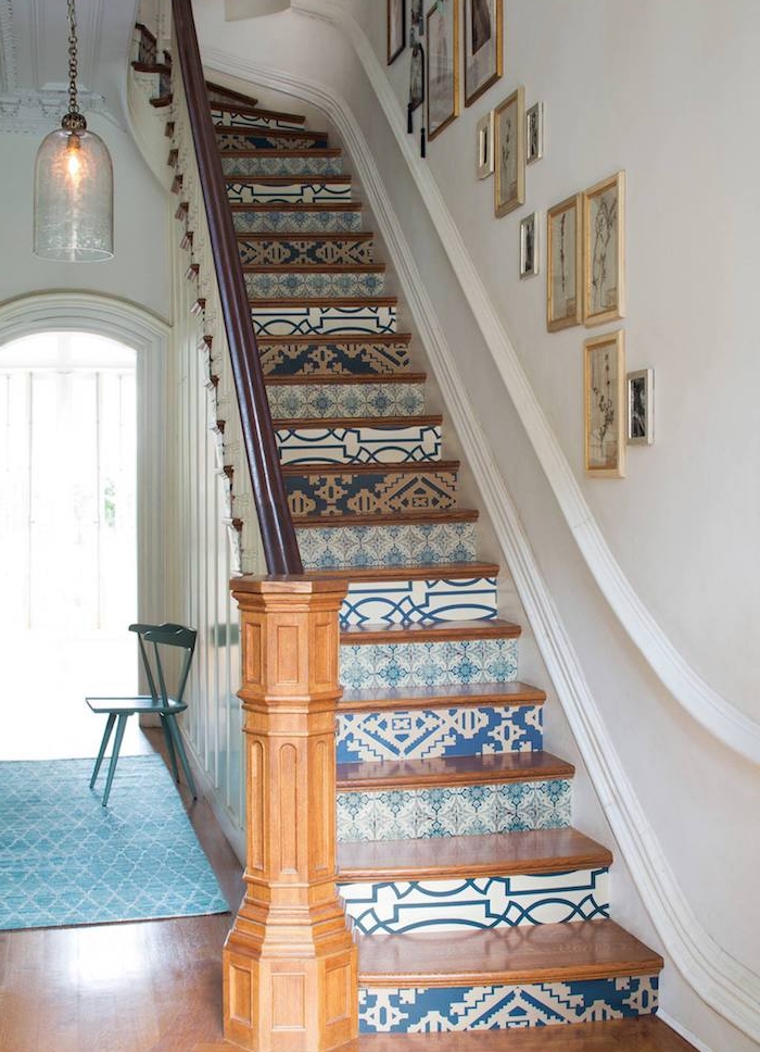 papier peint à motifs blancs, beiges et bleus sur les contremarches, marches et rambarde en bois, mur de cadres sur la montée d escalier, suspension originale
