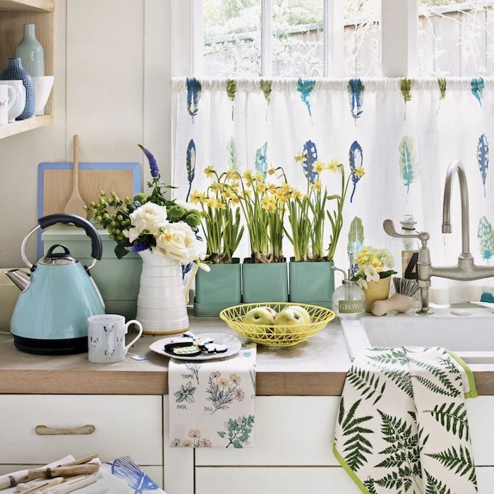 des accessoires deco bleu celadon, meuble cuisine blanc avec plan de travail en bois et étagères en bois, plusieurs plantes vertes, rideau à plumes bleues, vertes et violettes
