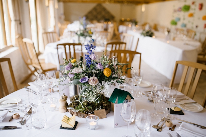deco table mariage dans un style champetre, nappe blanche, rondin en bois couvert de mousse, vase de fleurs, petite maisonnette en bois