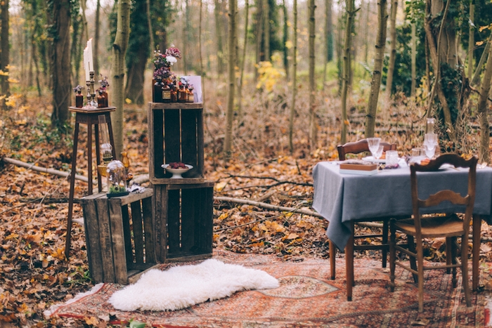mariage champetre dans un cadre forestier, tapis oriental, table et chaises en bois, cagette bois, fioles et bouteilles fleuries