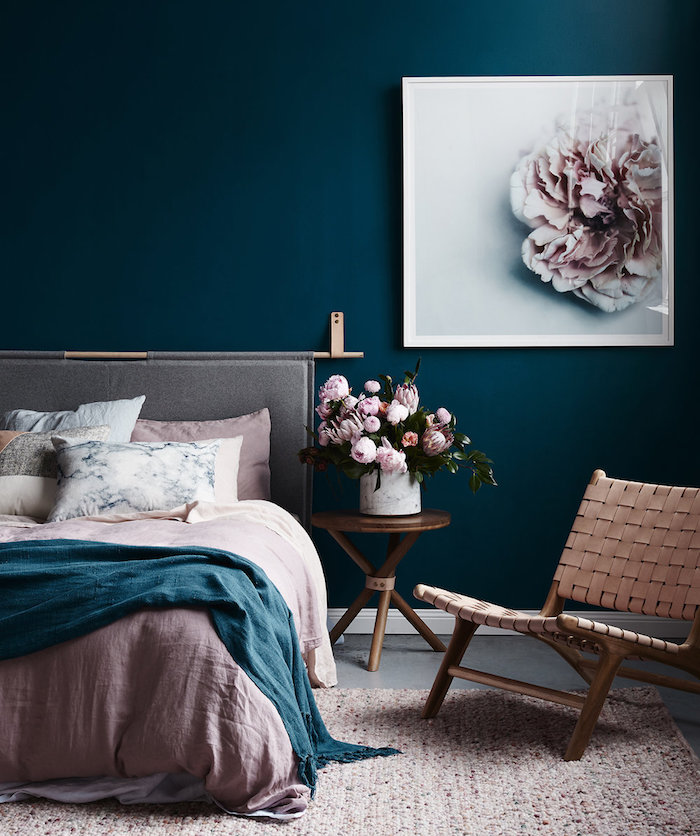 idée de deco chambre en rose et gris avec un mur de fond couleur bleu canard, nuance couleur pétrole, linge de lit et tapis rose, coussins effet marbre, bouquet de fleurs sur une table de nuit en bois