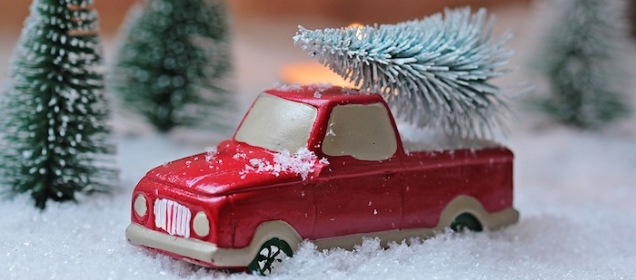 fond d ecran de noel en voiture miniature rouge sur une neige artificielle et sapins verts autour