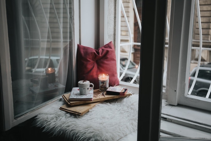 fond noel, de type hygge, un coussin d assise au bord d une fenêtre, plateau en bois avec livre, tasse de chocolat chaud et bougies romantique, coussin rouge