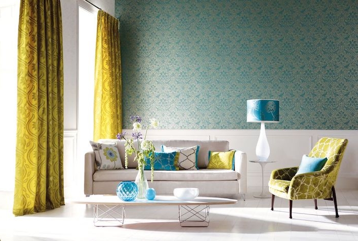 papier peint bleu petrole sur un pan de mur, canapé et table basse couleur blanche, sol blanc, rideaux jaunes baroques, petites touches de bleu turquoise