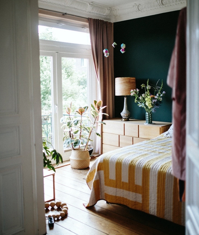 un seul pan de mur repeint de bleu petrole peinture, commode en bois, linge de lit blanc et jaune, parquet clair, plusieurs plantes vertes