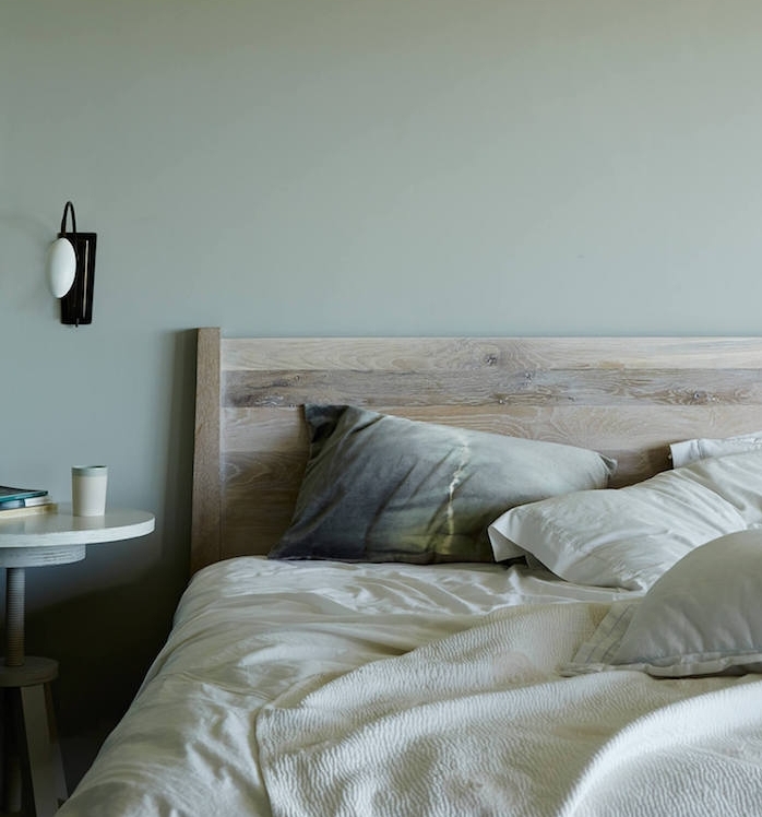 idée de peinture murale vert gris, lit en bois, linge de lit blanc, coussins gris, jaune et table en bois blanchie