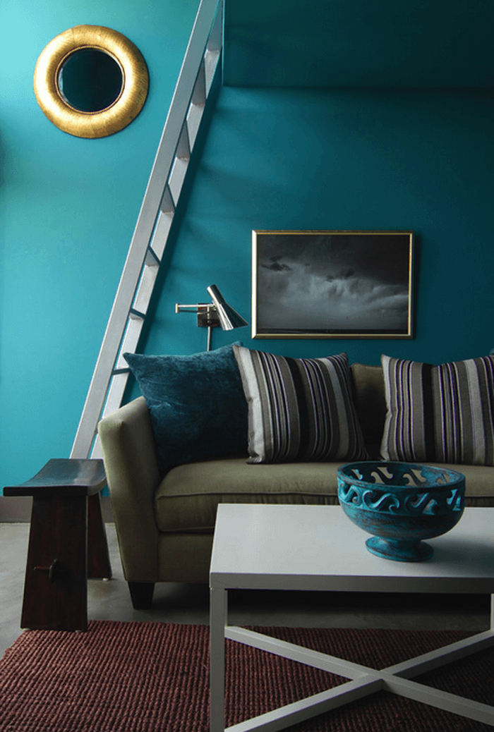 deco salon bleu canard comme choix de peinture murale, miroir rondm canapé vert olive, coussins canard, gris, noir et blanc, tapis rouge marron, table basse blanche