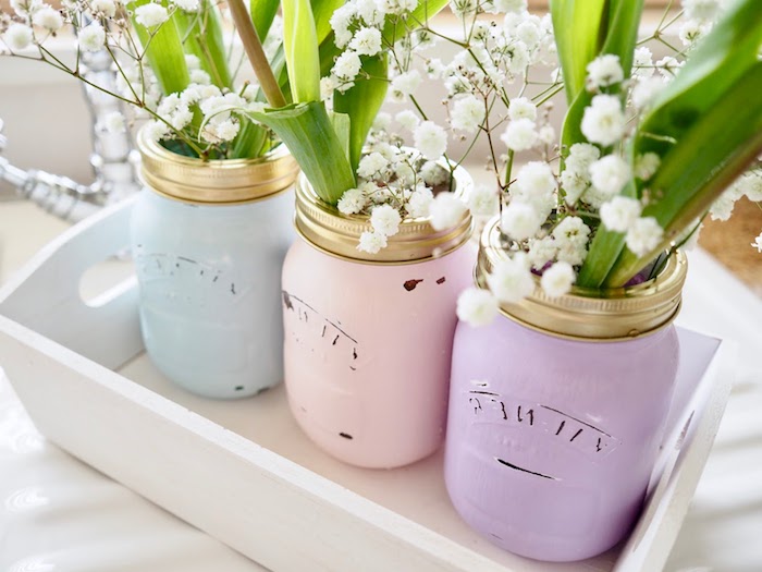exemple de diy mariage, des pots en verre recyclés et repeints de couleurs pastel, fleurs blanches, cagette blanchie