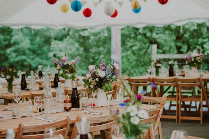 table et chaises en bois, deco mariage champetre, brocs avec des bouquets de fleurs, suspensions origami boules colorées