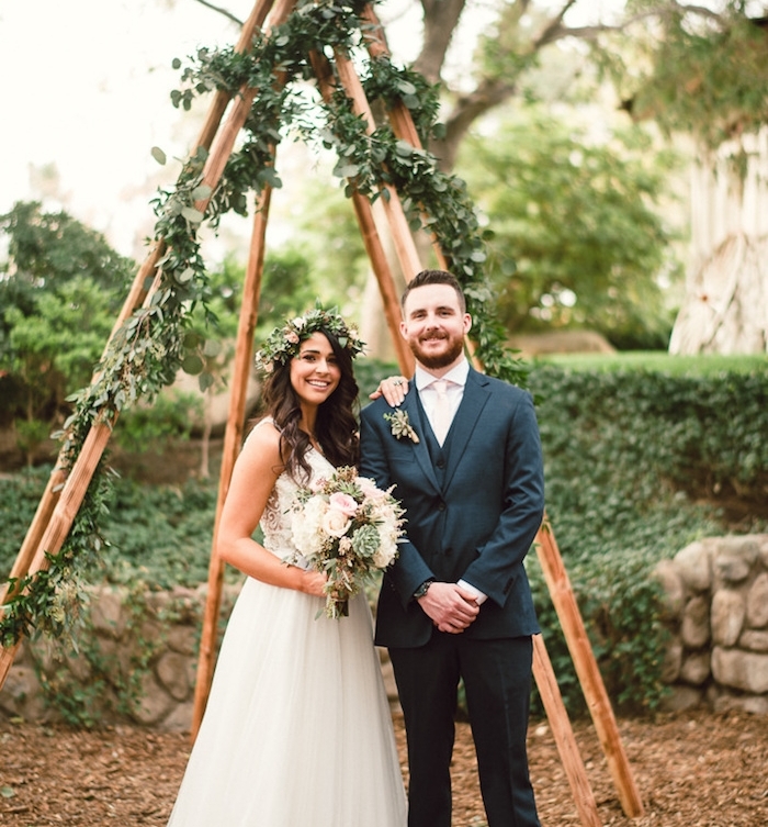 diy mariage, style champetre, tipi en bois avec decoration de guirlande feuillage verte, femme en robe champetre et bouquet de fleurs