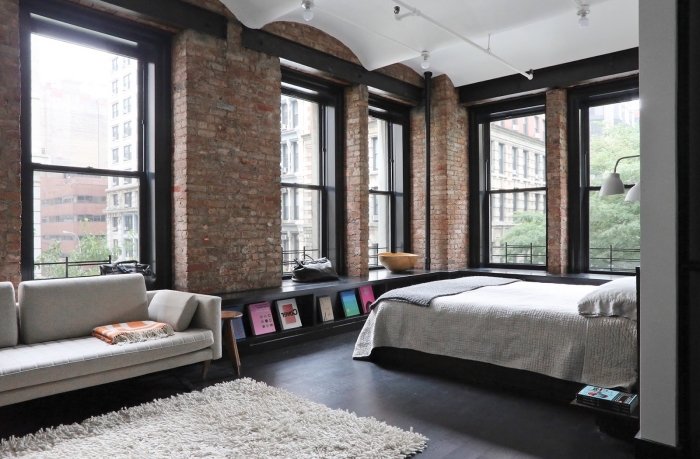 déco de chambre à coucher à design loft industriel aux murs briques et plafond blanc, tapis moelleux blanc sur plancher noir